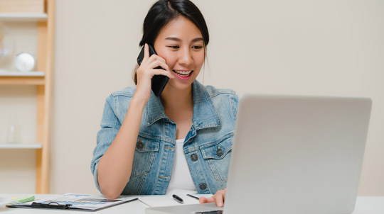 Woman using phone and looking at laptop